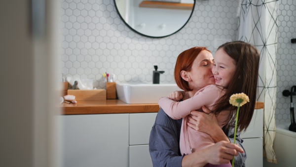 A little girl congratulates mother and gives her flower in bathroom at home.