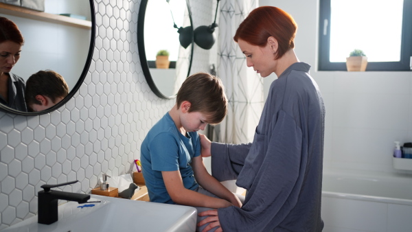 A mother consoling her little upset son in bathroom at home.