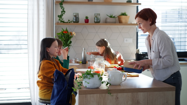 A mother of three little children preparing breakfast and lunch boxes in kitchen at home.