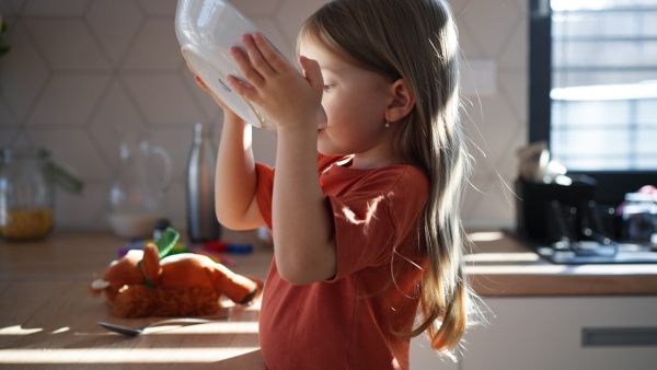 A little girl drinking soup from plate at home.