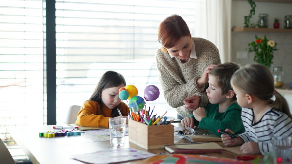 A mother of three little children supervising them when diong homework at home.