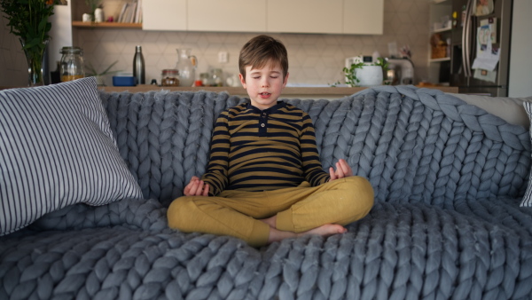 A little boy sitting on sofa and meditating at home.