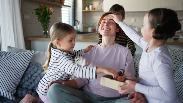 Three litttle children doing massage and apllying a make up to their mother at home.