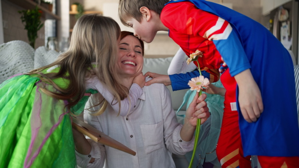 A mother of three little children in costumes getting present from them at home.