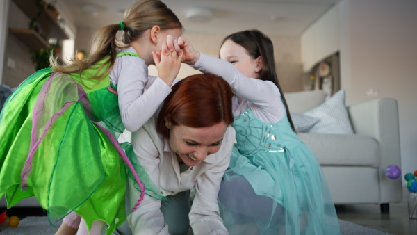 A happy mother having fun with little daughters in princess costumes at home.