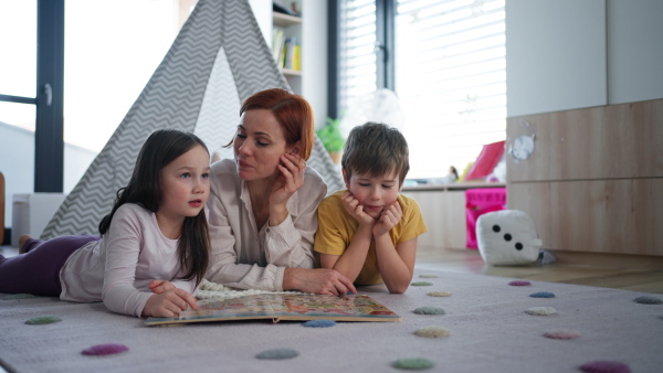 A cheerful mother of three little children reading them book at home.