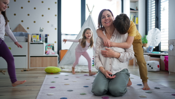 A cheerful mother of three little children receiving hugs from them at home.