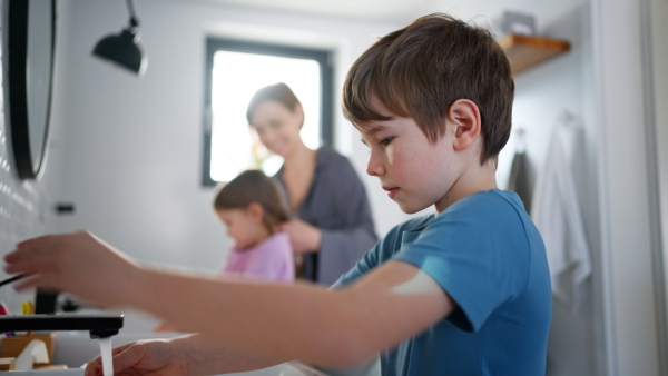 A mother supervising three little children in bathroom, morning routine concept.