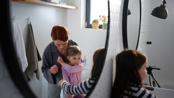 A mother combing her little daughter's hair in bathroom, morning routine concept.