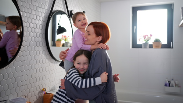 A mother hugging her little daughters in bathroom at home.