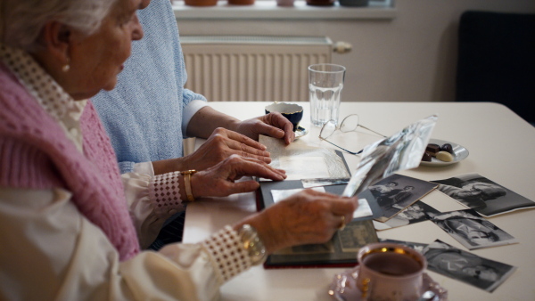 A senior mother with her adult daughter looking at old family pictures at home together