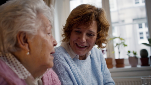 A senior mother with her adult daughter talking at home together