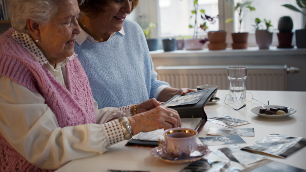 A senior mother with her adult daughter looking at old family pictures at home together