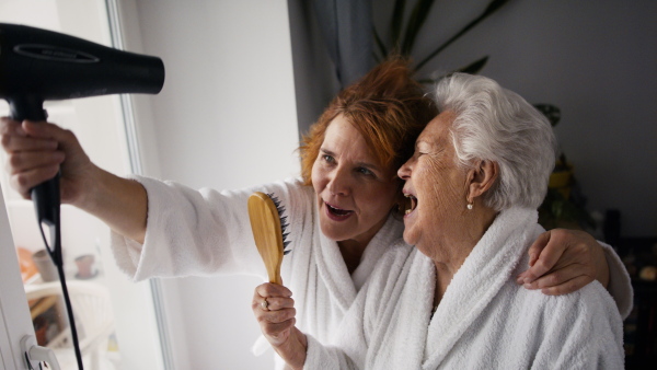 A senior mother with mature daughter in bathrobes having spa day at home together.