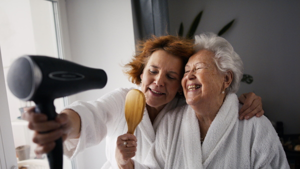 A senior mother with mature daughter in bathrobes having spa day at home together.