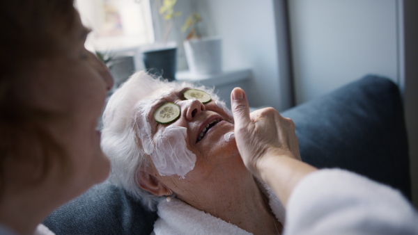 A senior mother with mature daughter in bathrobes having spa day at home together.