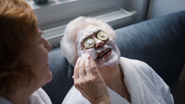 A senior mother with mature daughter in bathrobes having spa day at home together.