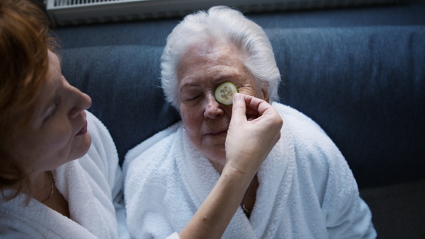 A senior mother with mature daughter in bathrobes having spa day at home together.