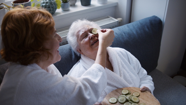 A senior mother with mature daughter in bathrobes having spa day at home together.