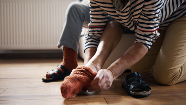 A nursing caregiver helps put on socks to senior woman at home.