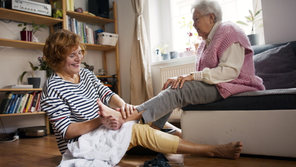 A senior woman getting foot massage from healthcare worker at home.