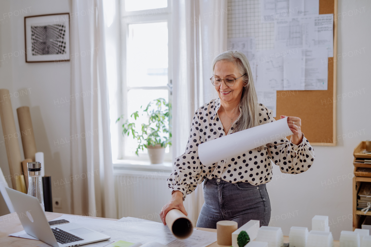 A woman architect pulling rolled-up blueprints out of tube in office.