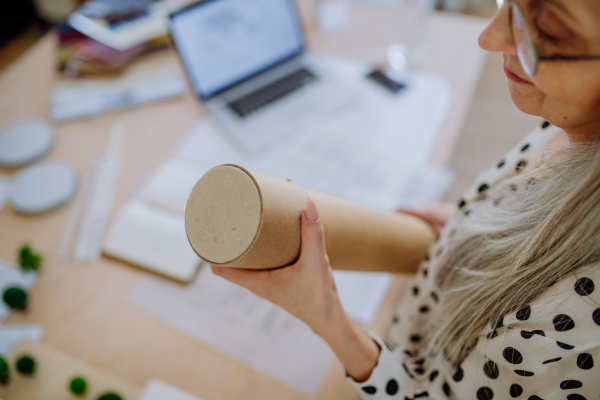 A close-up of woman architect pulling rolled-up blueprints out of tube in office.