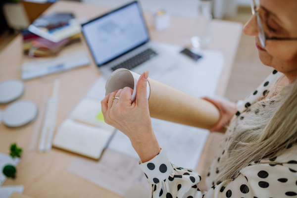 A close-up of woman architect pulling rolled-up blueprints out of tube in office.