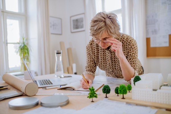 A senior woman eco architect with model of modern bulidings working in office.