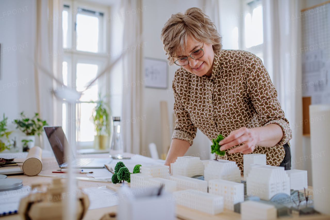 A senior woman eco architect with model of modern bulidings working in office.