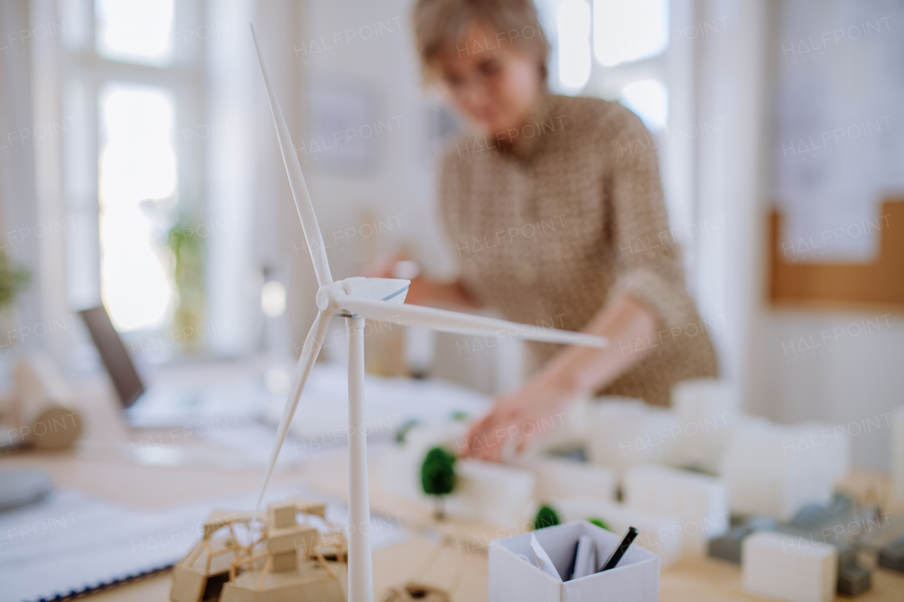 A senior woman eco architect with model of modern bulidings working in office.