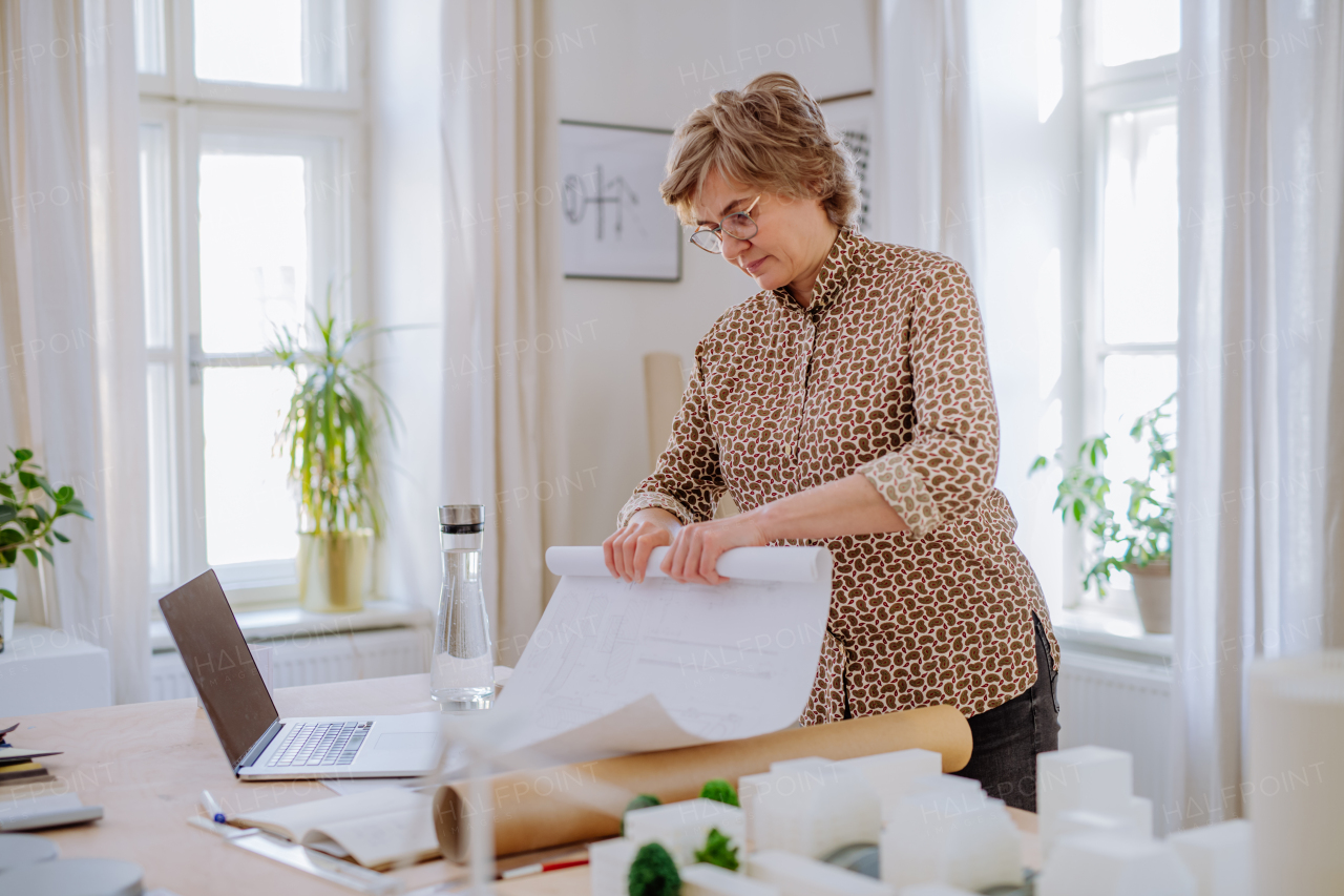 A mature woman architect rolling up blueprints in office.