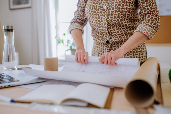 A close-up of woman architect rolling blueprints into tube in office.