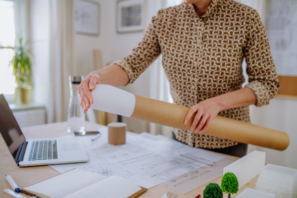 A close-up of woman architect putting rolled-up blueprints to tube in office.