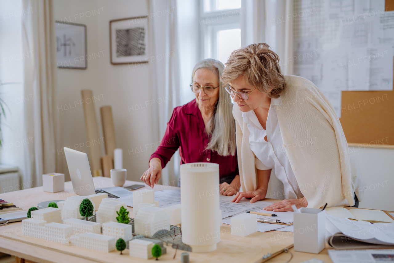 Mature women eco architects with model of modern bulidings and blueprints working together in an office.