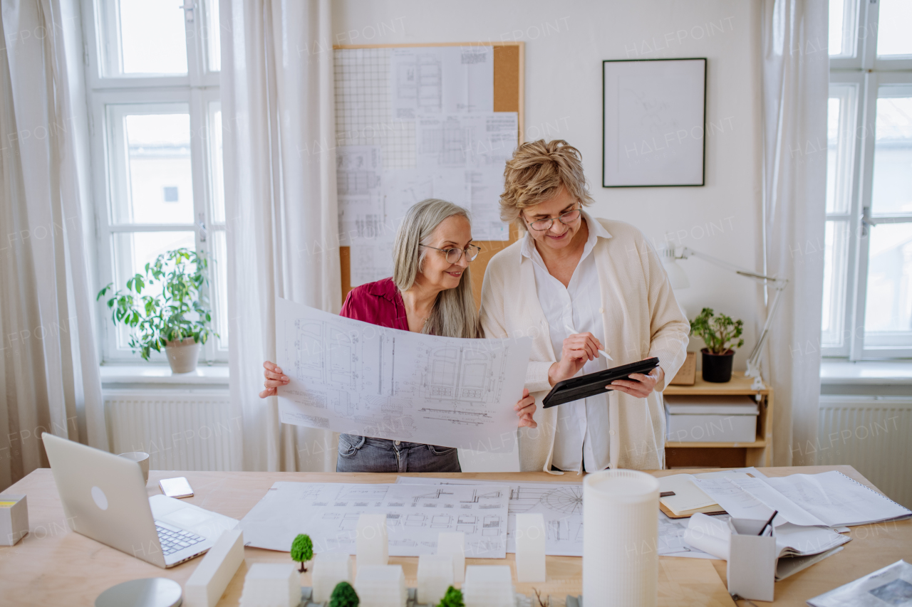 Senior women architects looking at the blueprints together in office .