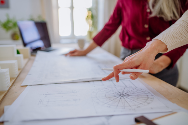 A close-up of mature women architects looking at blueprints together in office .