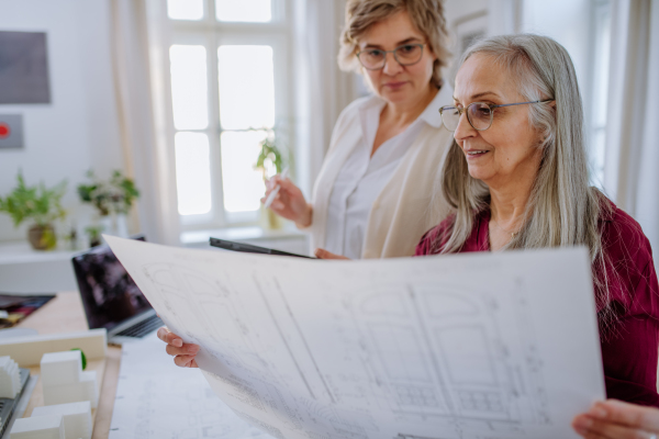 Mature women eco architects with model of modern bulidings and blueprints working together in an office.