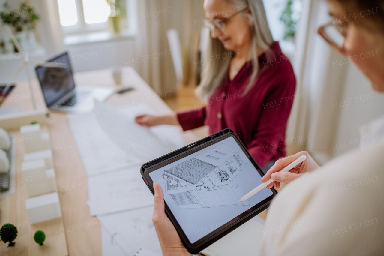 Mature women eco architects with blueprints working on a tablet together in office.