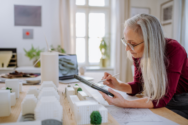 A senior woman eco architect with model of modern bulidings working in office.