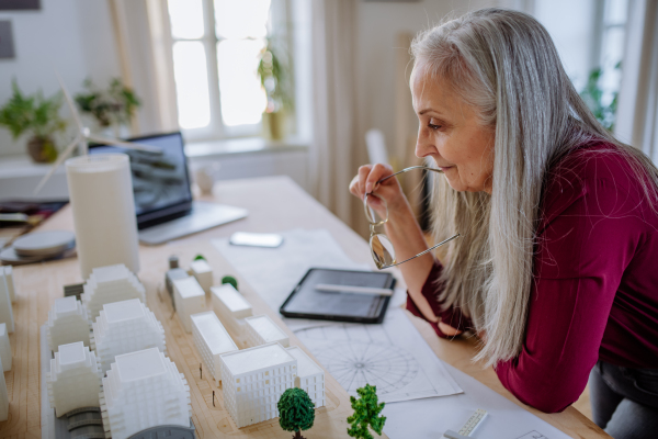 A senior woman eco architect with model of modern bulidings working in office.