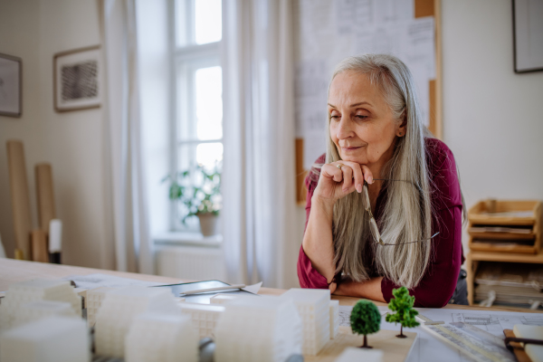 A senior woman eco architect with model of modern bulidings working in office.