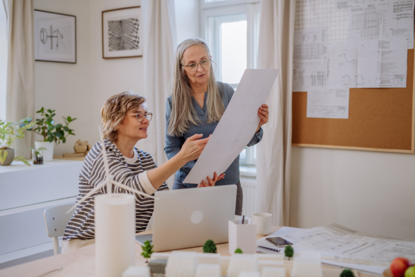 Mature women eco architects with model of modern bulidings and blueprints working together in an office.