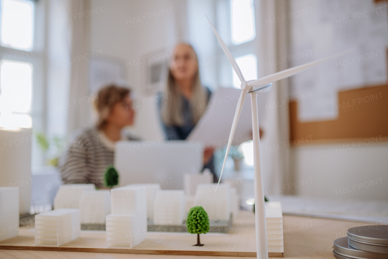 Women eco architects working together in office, with a wind turbine in foreground.