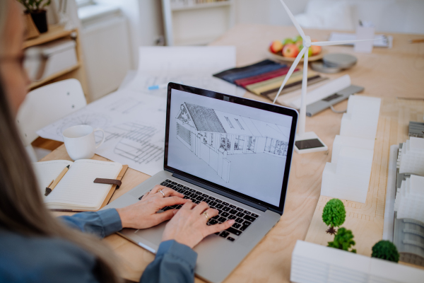 A close-up of senior woman eco architect designing modern bulding on lapotp in office.