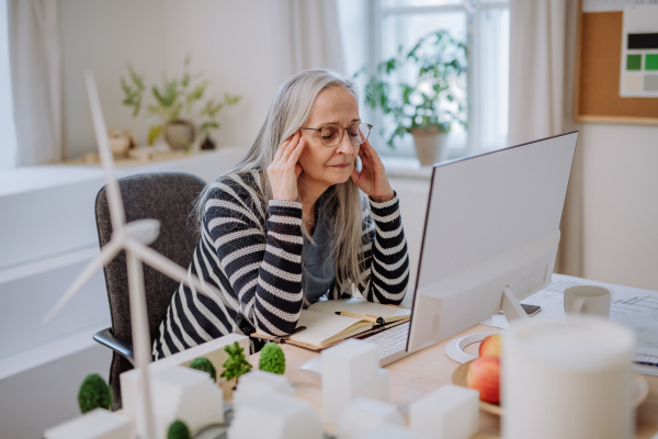 A mature business woman with working on laptop in office and having headache.