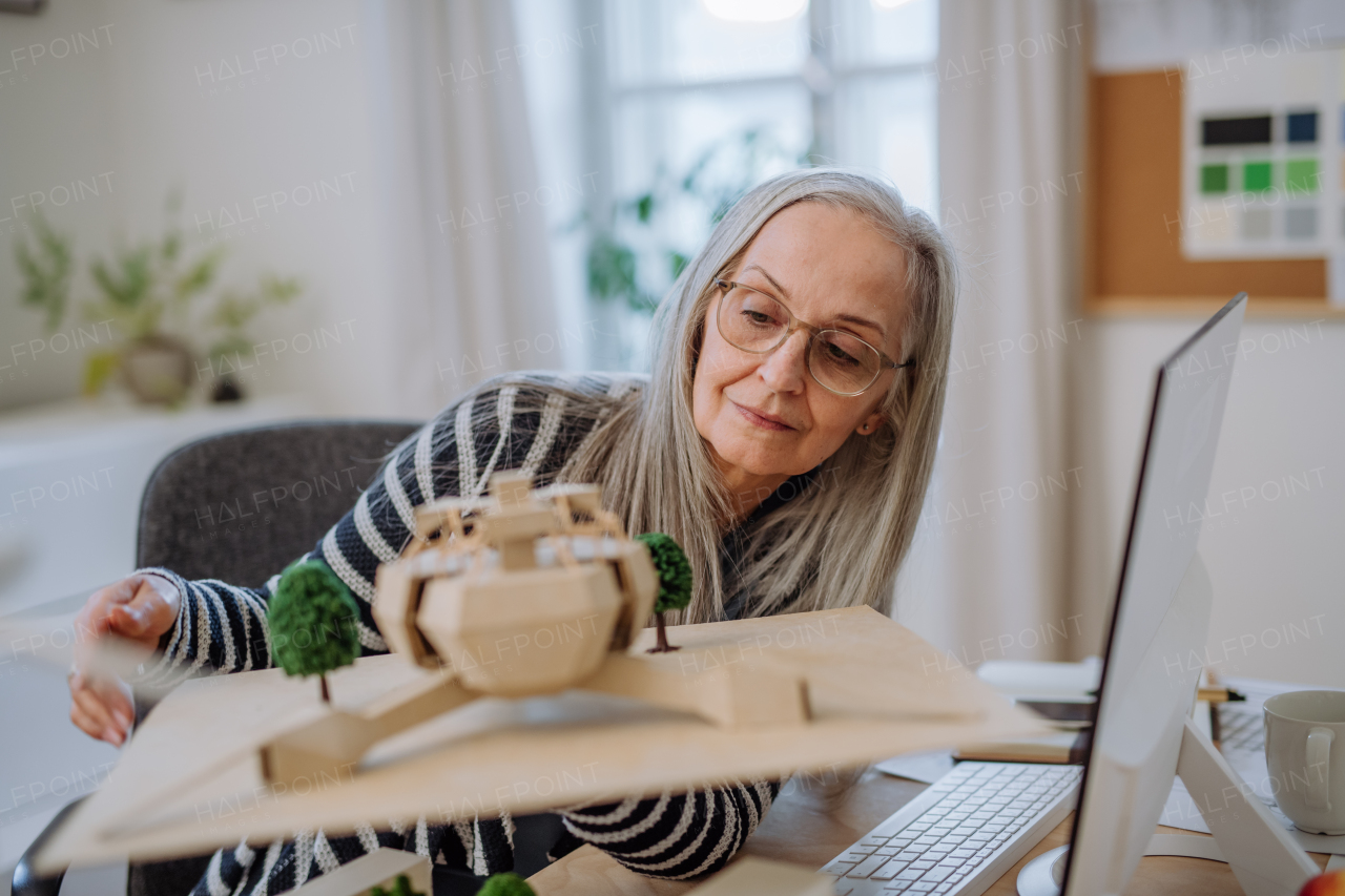 A senior woman architect holding model of modern eco buliding in office