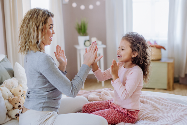 A happy mother with her little daughte playing clapping hands game on bed at home.