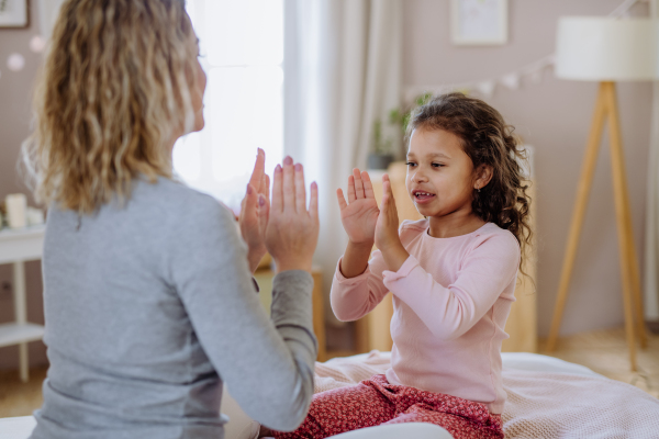 A happy mother with her little daughte playing clapping hands game on bed at home.