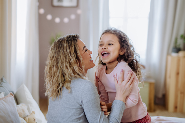 A happy mother with her little daughter hugging and having fun together on bed at home.